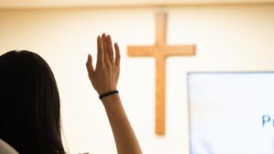 A woman raises her hand in front of a cross.